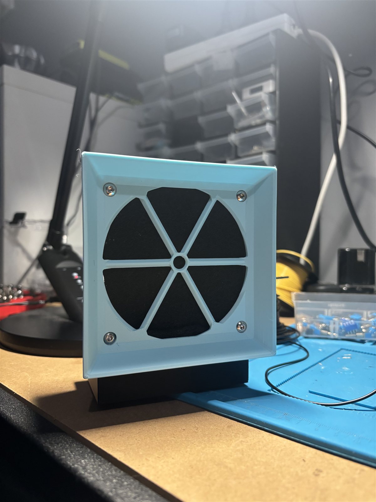 Blue 3D-printed bench fume extractor with a square front grille on an electronics workbench