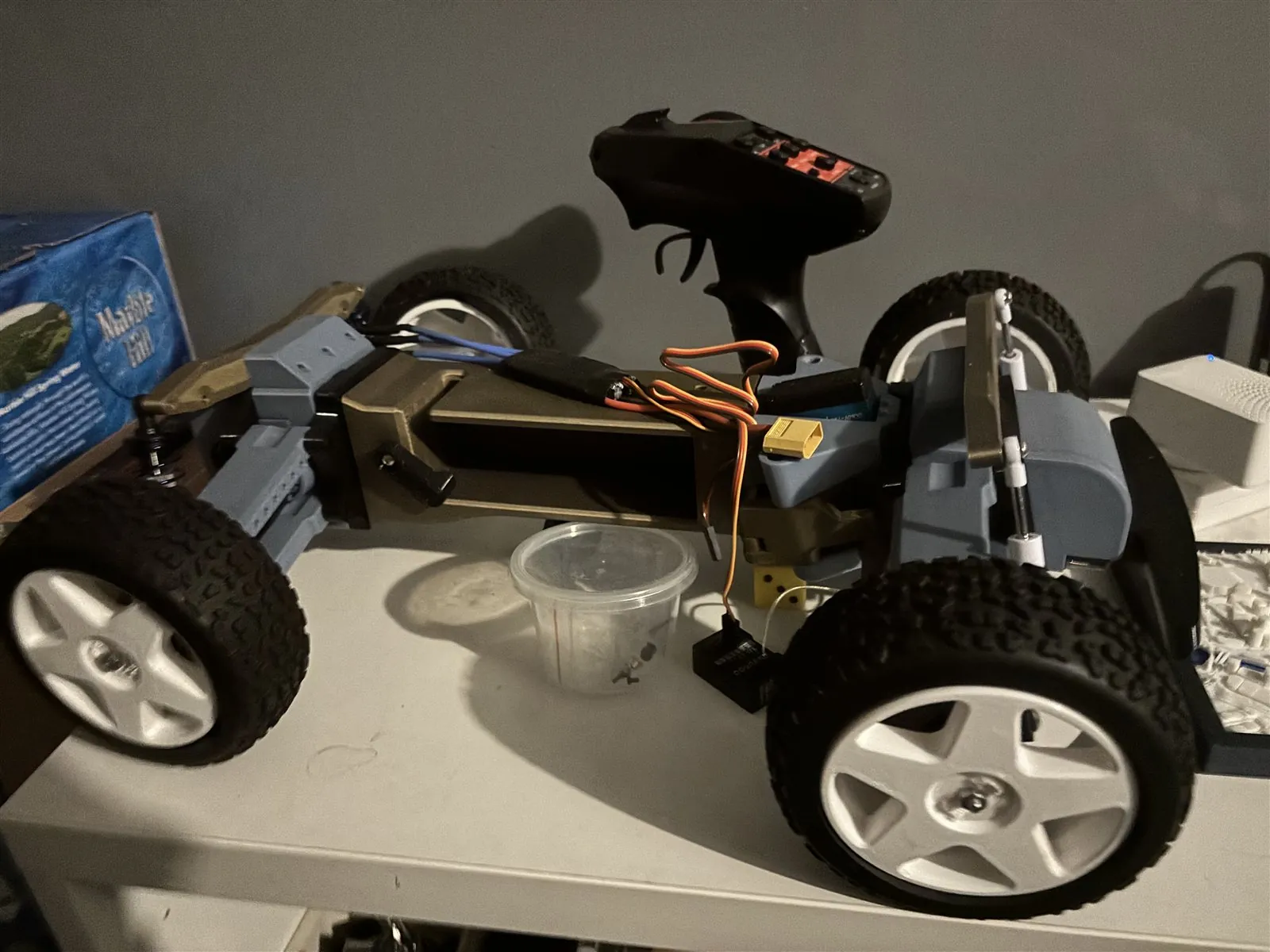 Partly assembled 3D-printed TARMO5 RC car with visible wiring and a handheld transmitter